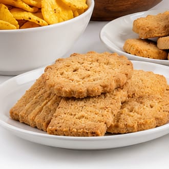 Plates of tea biscuits and coconut sweets beside a bowl of crisps.