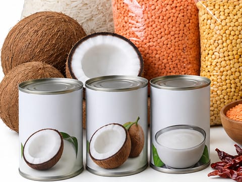 Whole and halved coconuts beside cans of coconut milk and coconut cream.